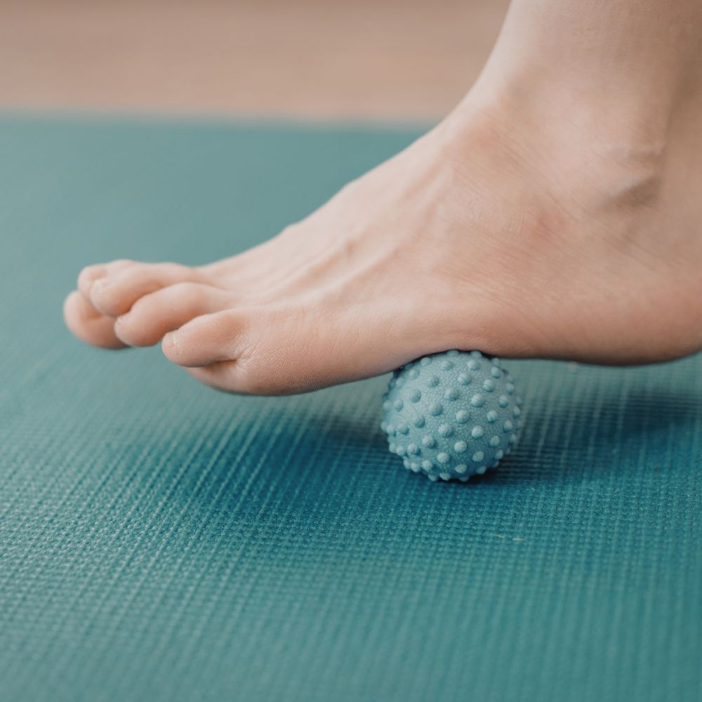Bare foot rolling on spiky massage ball on teal yoga mat